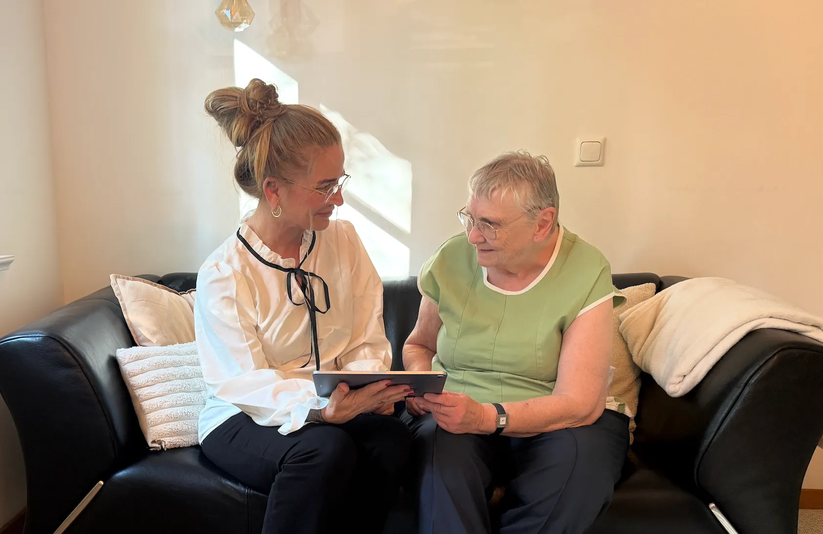 Fürsorgliche Betreuerin hilft einer älteren Dame beim Aufstehen in einem hellen Wohnzimmer